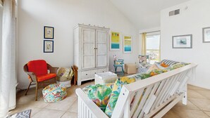 A bright, well-lit room with a white crib, a wicker chair, a white cabinet, and a colorful cushion. - Walk to the Sand! Ocean-View Galveston Townhome (Galveston)