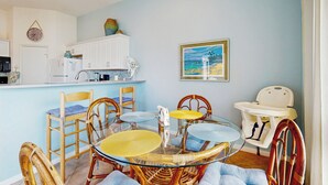 A dining area with a glass table surrounded by wicker chairs, a white cabinet, and a baby high chair. - Walk to the Sand! Ocean-View Galveston Townhome (Galveston)