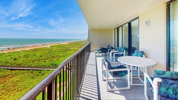 Een balkon met uitzicht op het strand, witte tuinmeubels en een glazen deur.