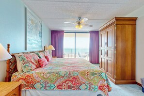 A bedroom with a large bed, a ceiling fan, a wardrobe, and a balcony with purple curtains. - Gulf Views, Resort Perks: Suntide III - Unit 703 (South Padre Island)