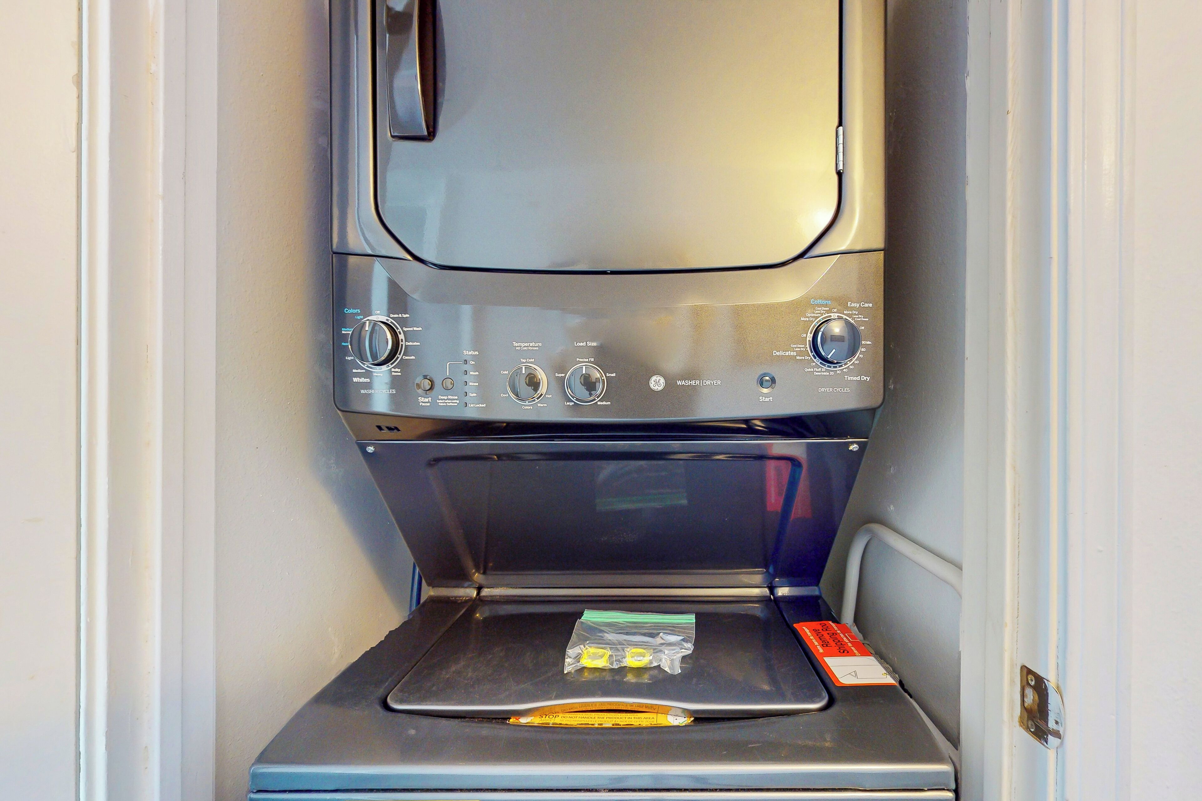 Lavadora compacta y moderna con panel de control que ofrece múltiples opciones y un pequeño paquete de detergente en la puerta.