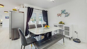 A modern dining area with a marble table, black chairs, and a bench. There is a refrigerator, a trash bin, and a cabinet with decorative items. - Steps to Sea! Coastal Escape in Fort Walton Beach (Fort Walton Beach)