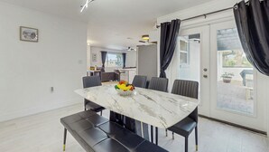 A modern dining area with a marble table, black upholstered chairs, and a fruit bowl centerpiece. - Steps to Sea! Coastal Escape in Fort Walton Beach (Fort Walton Beach)