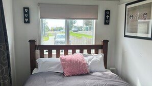 A bedroom with a bed, a window, and a view of the street. - Family Beach House - Prime Location (Riversdale Beach)