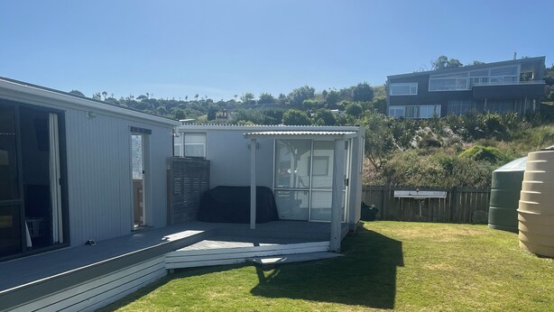 A modern house with a patio area, a covered outdoor seating area, and a view of a hillside. - Family Beach House - Prime Location (Riversdale Beach)