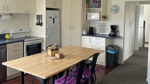 A compact kitchen with a wooden table, black chairs, a refrigerator, a microwave, and a coffee maker. - Family Beach House - Prime Location (Riversdale Beach)