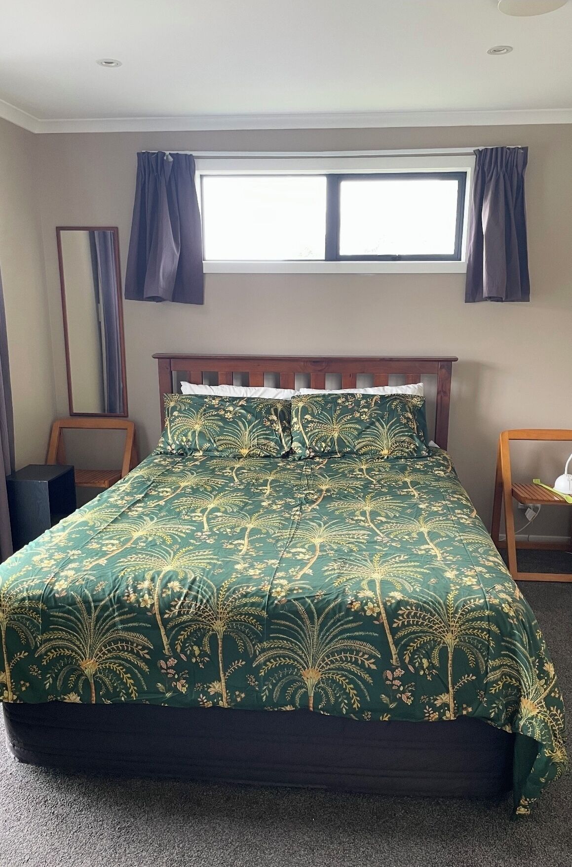A bedroom with a bed, a window with curtains, a mirror, and a bedside table.