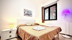 Una camera da letto con un letto, un comodino, una lampada, una finestra e un quadro appeso al muro.