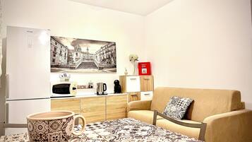 A compact living space with a kitchenette, a dining area with a patterned tablecloth, a sofa with a patterned cushion, and a wall-mounted picture.