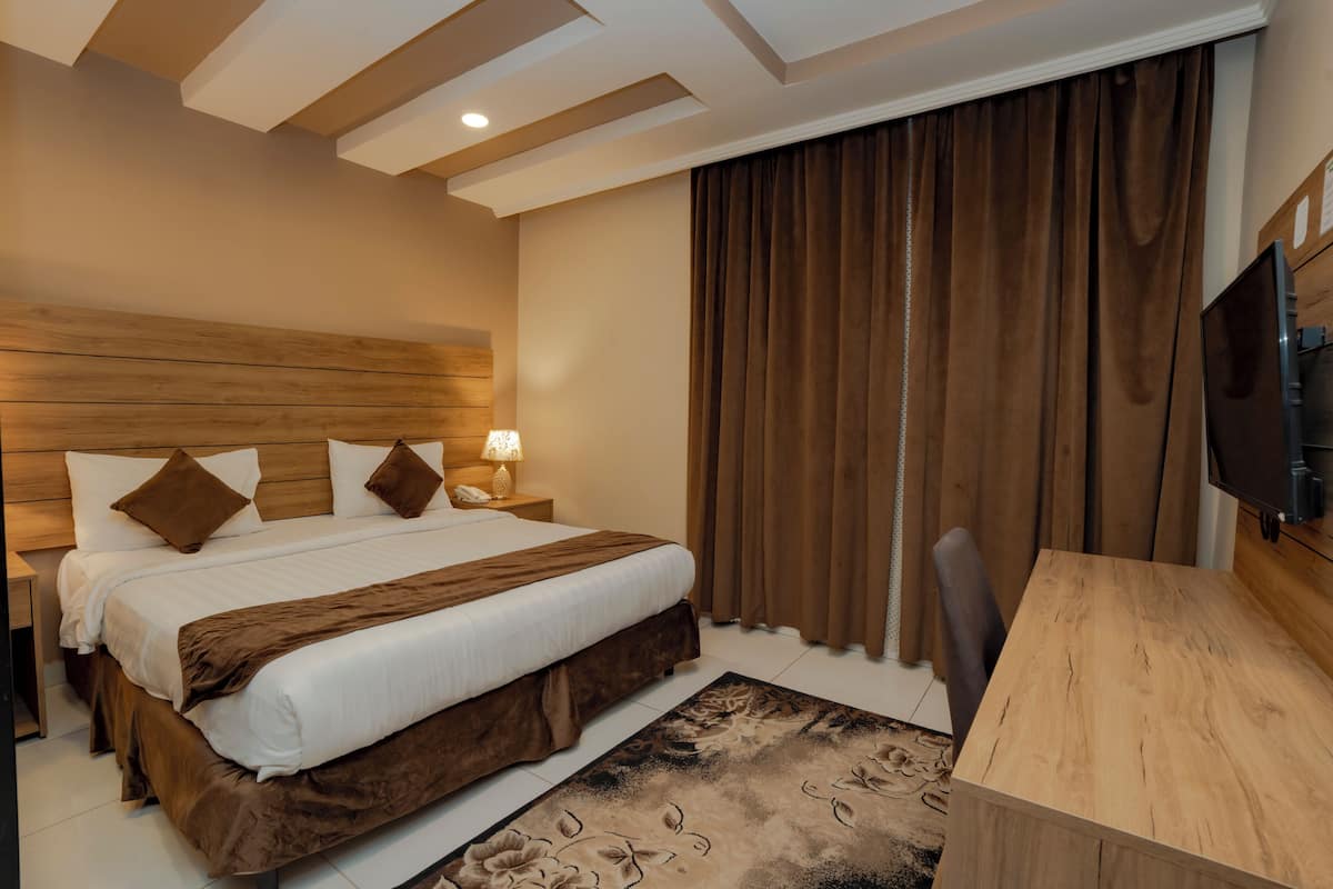 A hotel room with a bed, bedside table, lamp, curtains, and a TV.