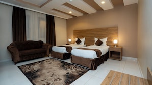 A hotel room with a sofa, two beds, a nightstand with a lamp, and a floral rug. - MG Crown Hotel 4 (Madinah)