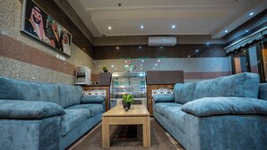 A modern living room with two blue sofas, a wooden coffee table, and a decorative plant. - MG Crown Hotel 4 (Madinah)