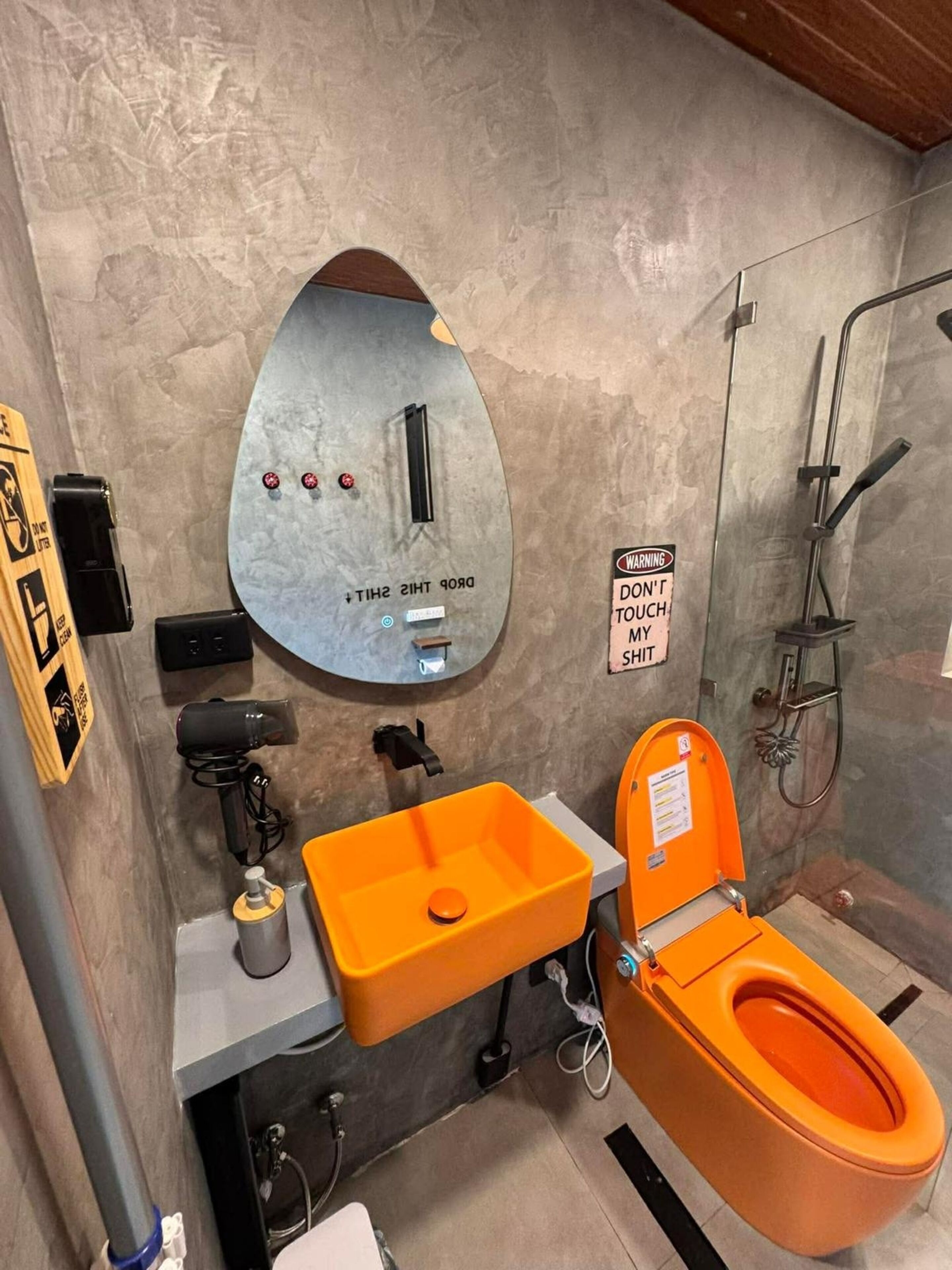 A bathroom with a large mirror, an orange sink, and a toilet.