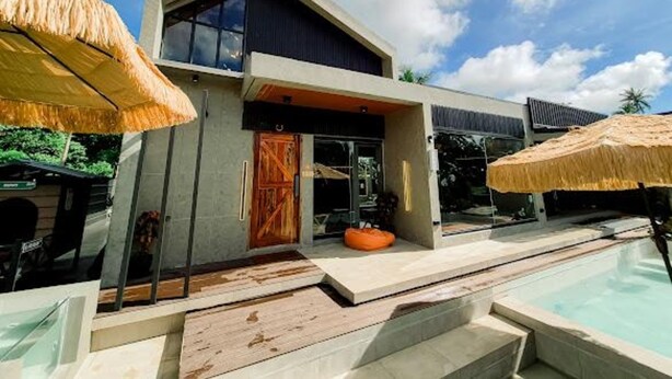 Een modern huis met een zwembad, een houten deur en rieten parasols.