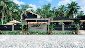 Mamay's Privé Villa met rieten dak, omringd door palmbomen en een grindpad.
