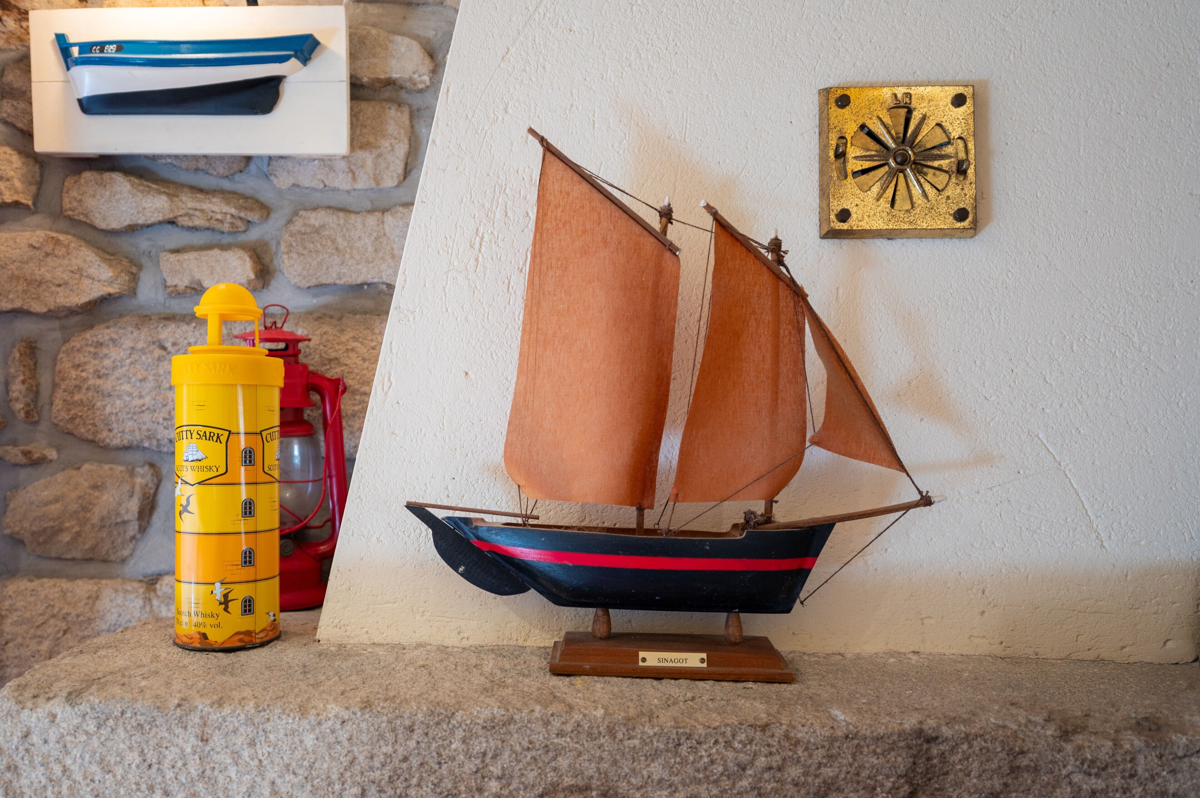 A model sailboat on a stand, a yellow container, and a compass on a wall.