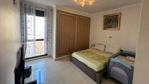 Une chambre à coucher comprenant un lit, un petit bureau, une armoire et une fenêtre avec des rideaux.