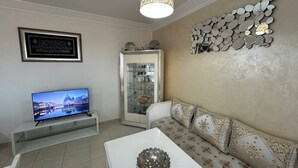 Un salon doté d’un téléviseur à écran plat, d’une table basse blanche, d’un canapé à motifs, d’un élément décoratif mural et d’une vitrine contenant des objets décoratifs.
