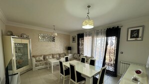 Un coin repas avec une table et des chaises blanches, un canapé et un meuble avec des portes en verre.