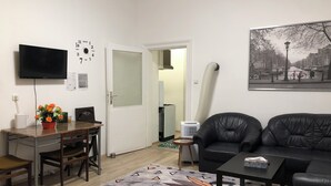 Ett modernt vardagsrum med en svart lädersoffa, ett soffbord, en matplats med bord och stolar, en tv som är monterad på väggen och en tavla som föreställer en stadsbild.