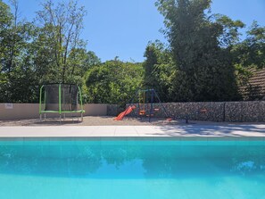 A swimming pool with a slide and swings, surrounded by trees and a stone wall. - Vacation home Josipa by Interhome (Vrgorac)