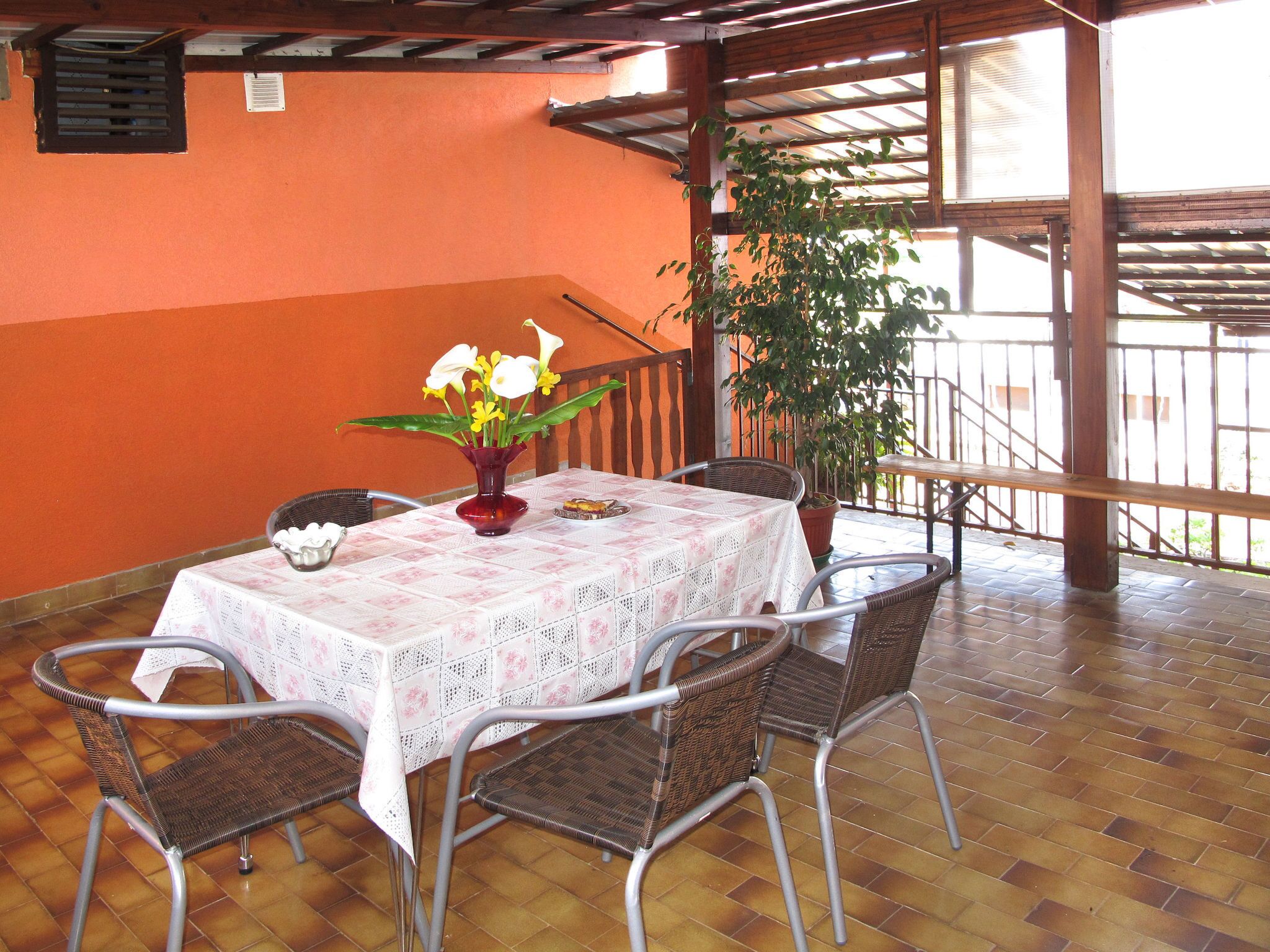A covered patio with a table and chairs, a vase with flowers, and a potted plant.