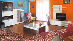 A living room with a giraffe-patterned sofa, a rocking chair, a glass coffee table, a television, and a bookshelf. - Lina (PUL305) by Interhome (Pula)