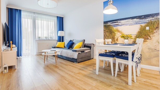 Un salon moderne avec un canapé, une table basse et une table à manger. Une grande fenêtre offre une vue sur la plage.