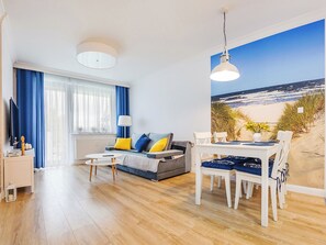 A modern living room with a sofa, coffee table, and dining table. There is a large window with a beach view. - Bliżej Morza by Interhome (Kolobrzeg)