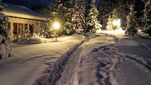 Ein verschneiter Pfad führt zu einem Gebäude mit schneebedecktem Dach und einem beleuchteten Laternenpfosten.