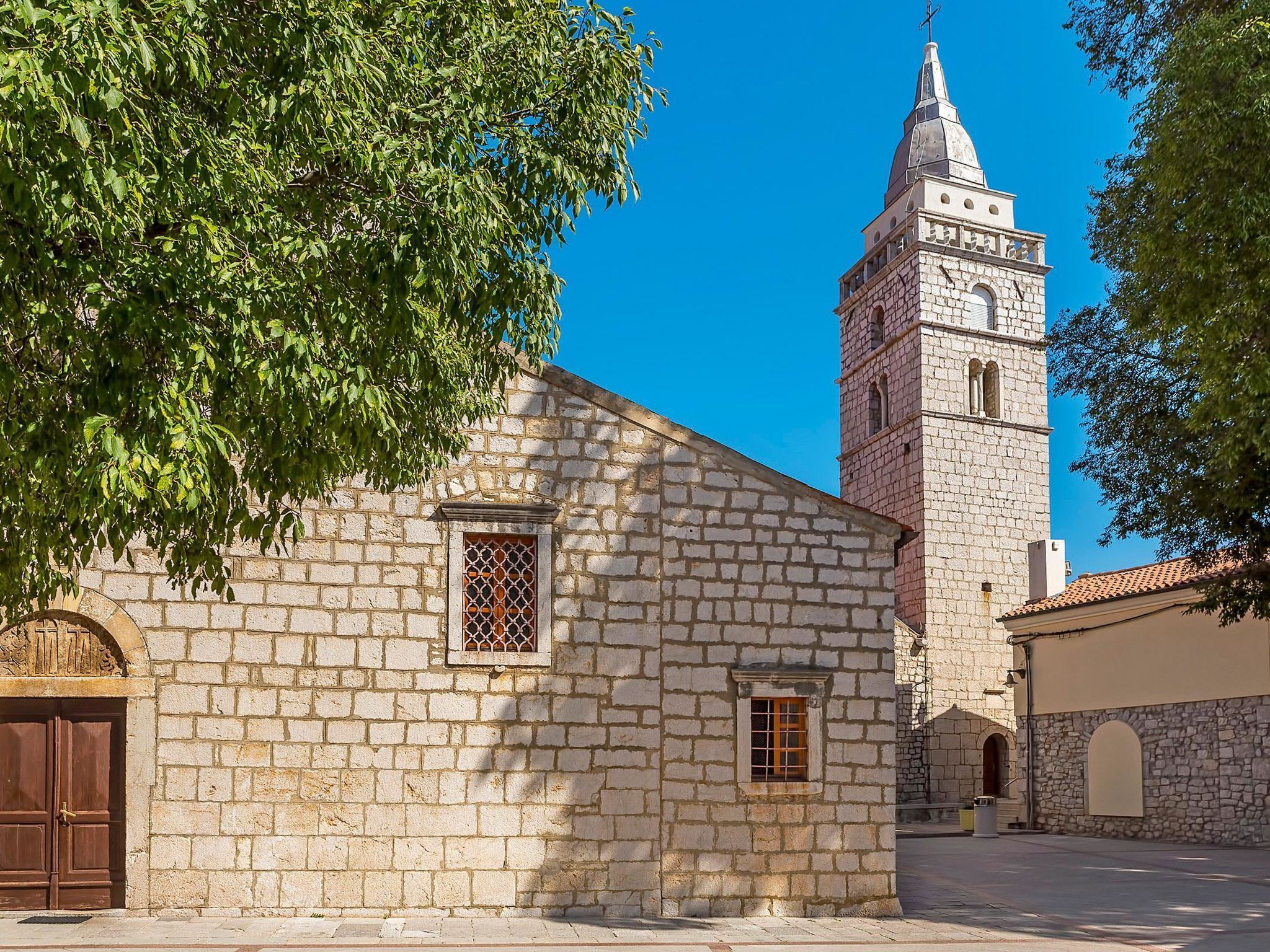 A stone building with a tower, a wooden door, and a window with a lattice design.
