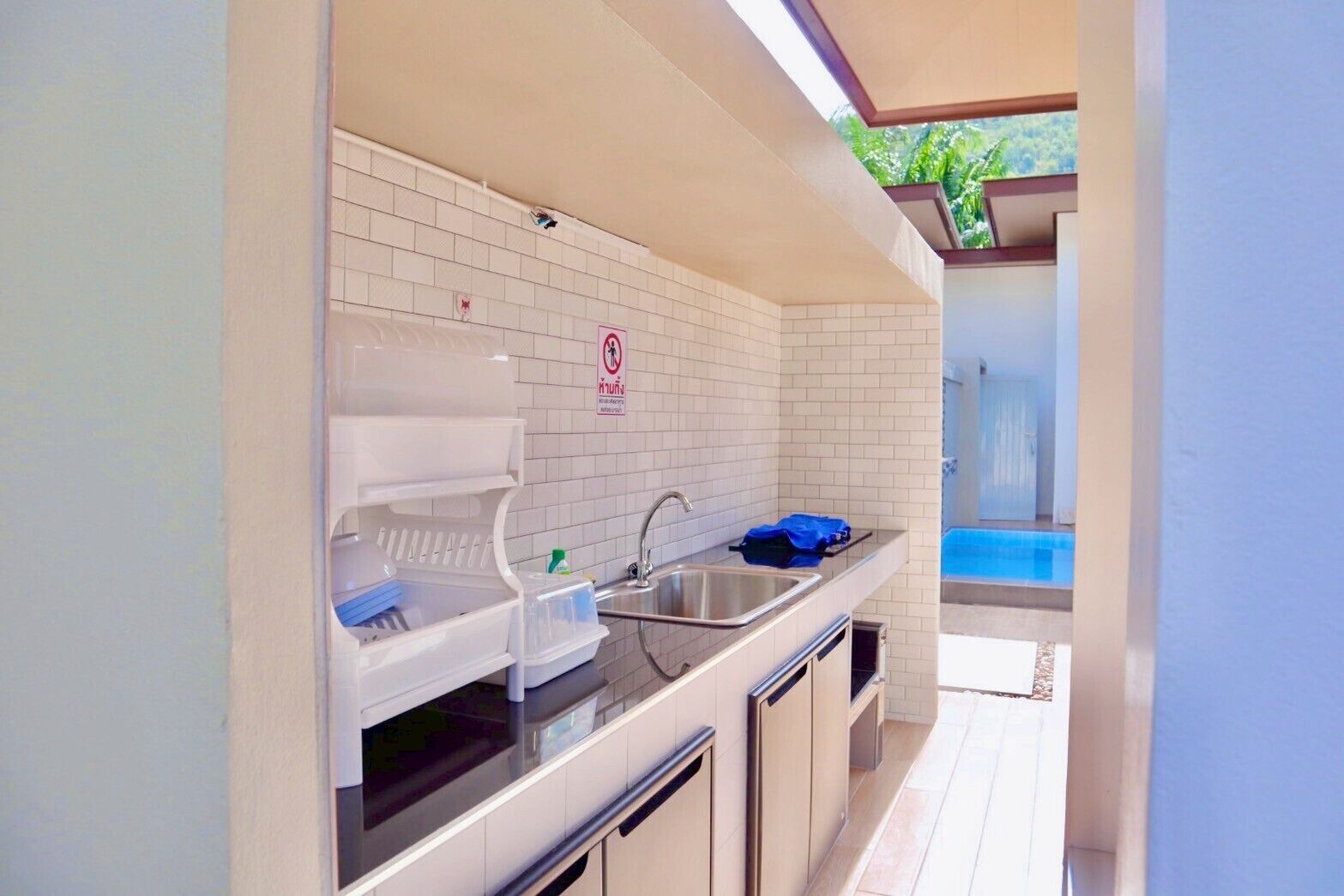 A modern kitchen with white tiles, a sink, and a countertop. There is a blue bag on the counter and a sign on the wall.