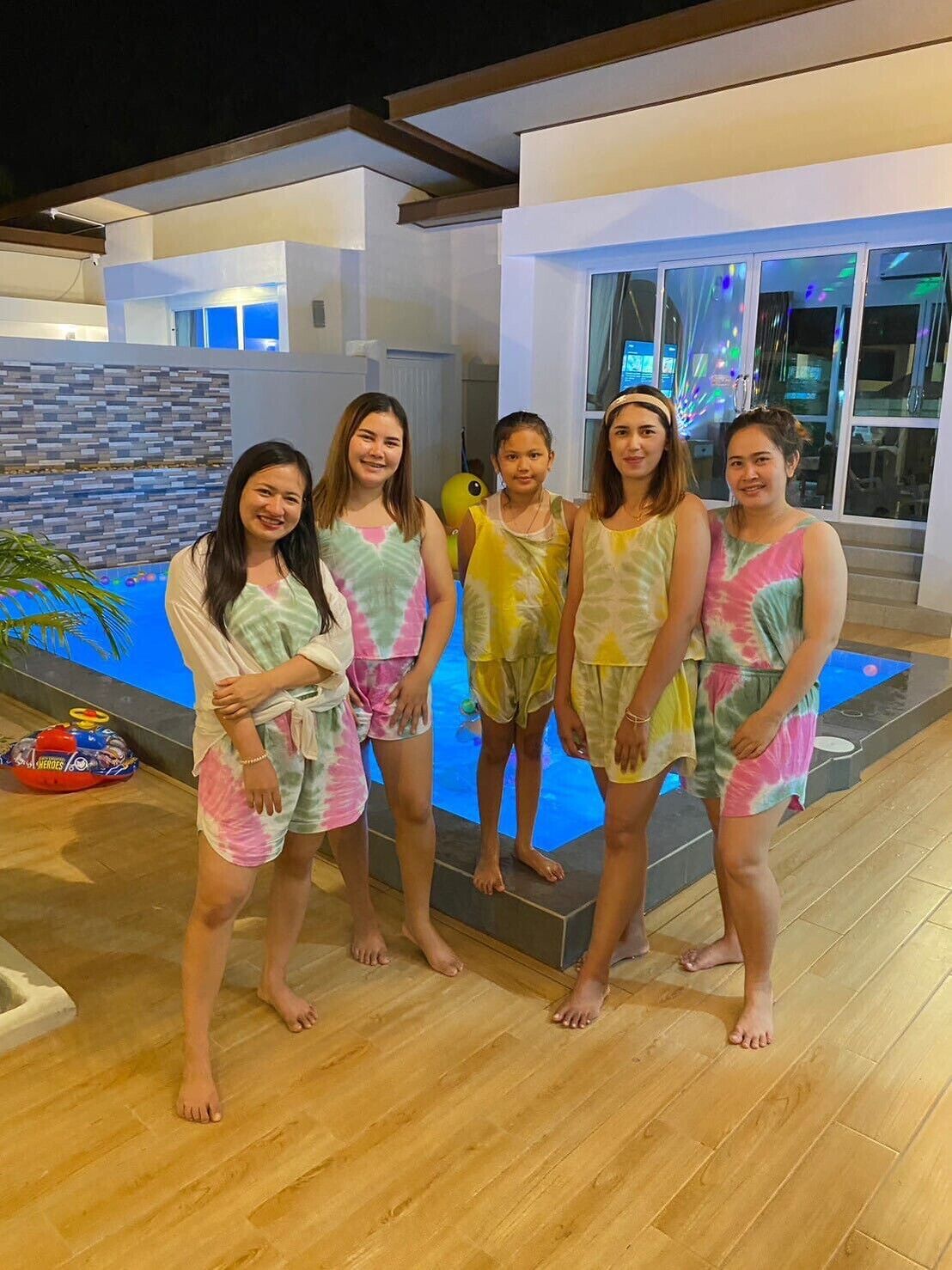 A group of people standing by a swimming pool with a modern building in the background.