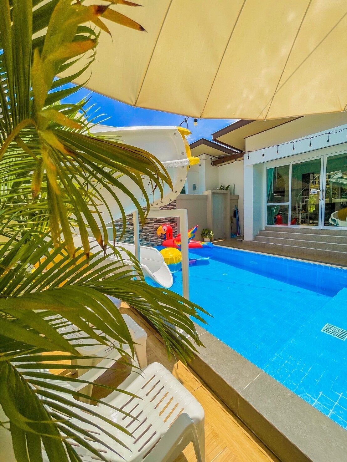Una piscina con tobogán, rodeada de palmeras y una zona techada.