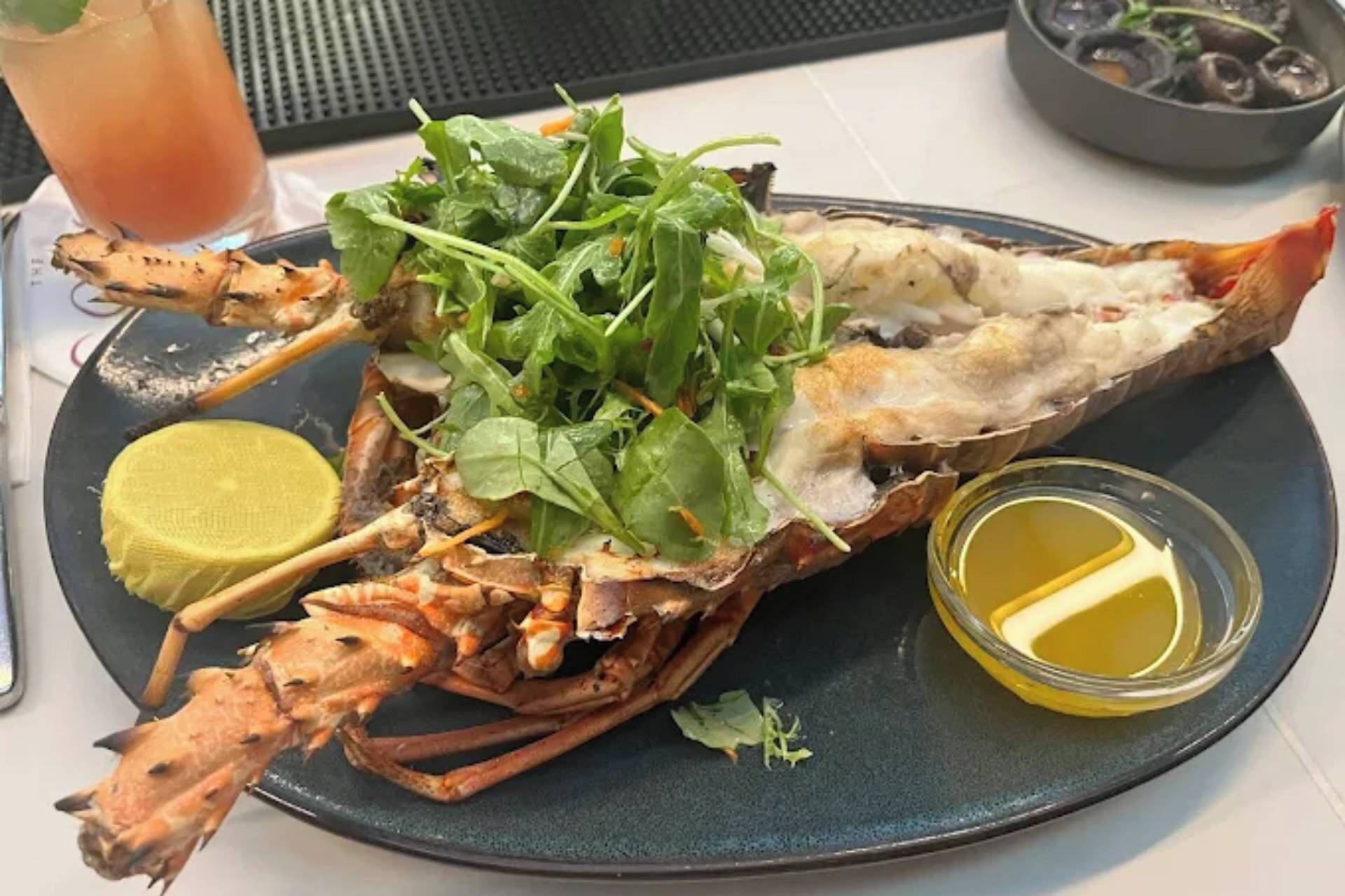Ein Fischgericht mit einem ganzen Hummer, Salat, Zitrone und einer Soße auf einem Teller.