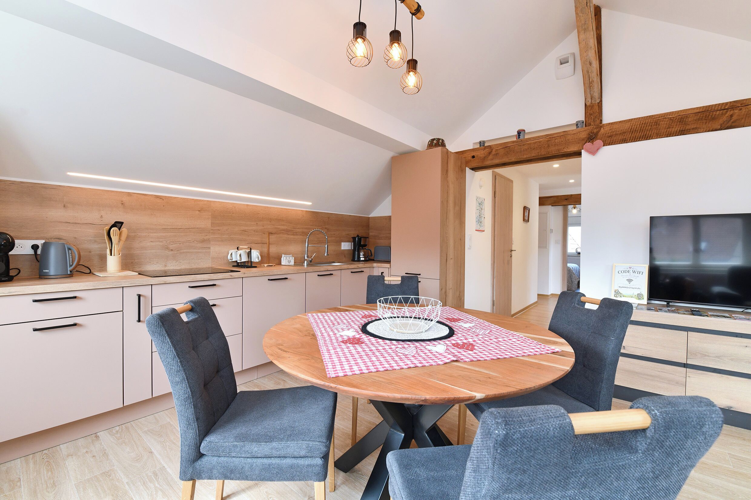 A modern kitchen with wooden accents, a dining area with a round table and chairs, and a flat-screen TV.