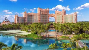 A large resort with multiple high-rise buildings, a central archway, and a pool area surrounded by palm trees. - Harborside Resort - 3 Bedroom - Full Resort Access (Paradise Island)