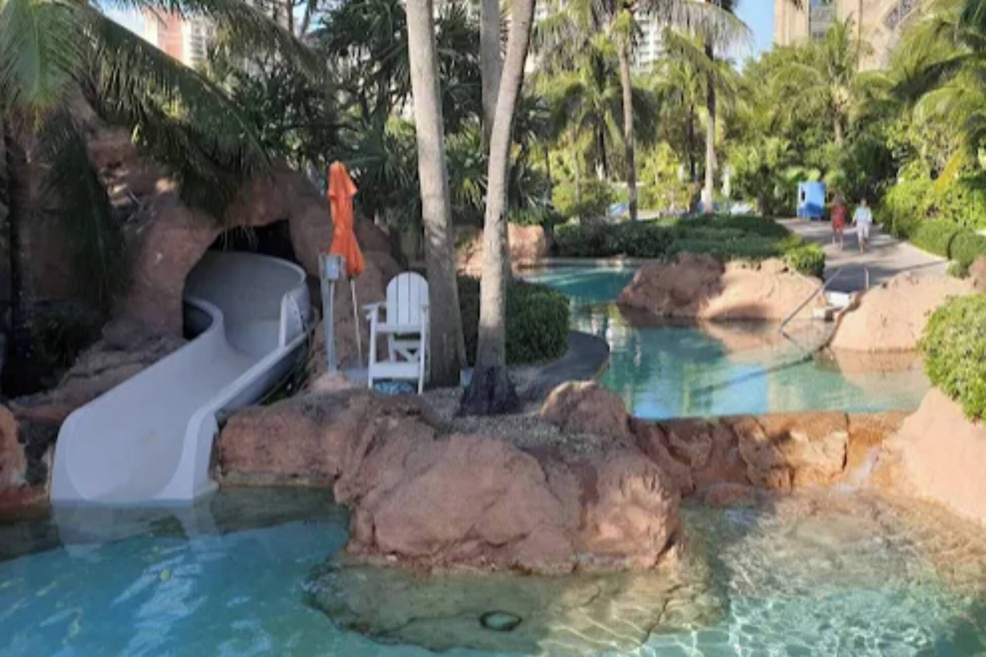 Zona de piscina con tobogán de agua, sillas de descanso y palmeras.