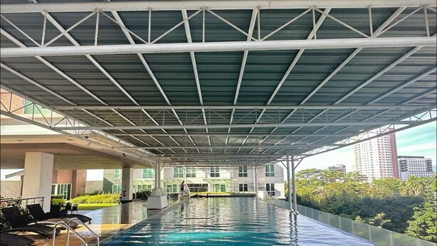 A large indoor swimming pool with a covered roof, surrounded by lounge chairs and a landscaped area.