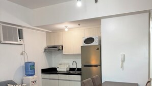 A compact living space with a kitchenette, a dining area with a table and chairs, a sofa with a patterned pillow, and a water dispenser.