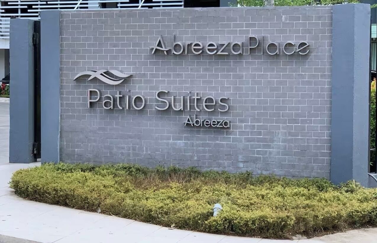 A sign for 'Areeza Place Patio Suites' with a wave design and a hedge in front.