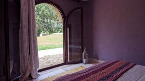 Ein Schlafzimmer mit großem Fenster, einem Bett, einem Nachttisch und einer Lampe.