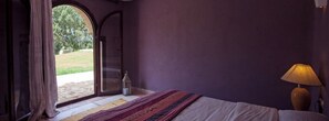 A bedroom with a large window, a bed, a nightstand, and a lamp. - Villa Gonatouki (ESSAOUIRA)