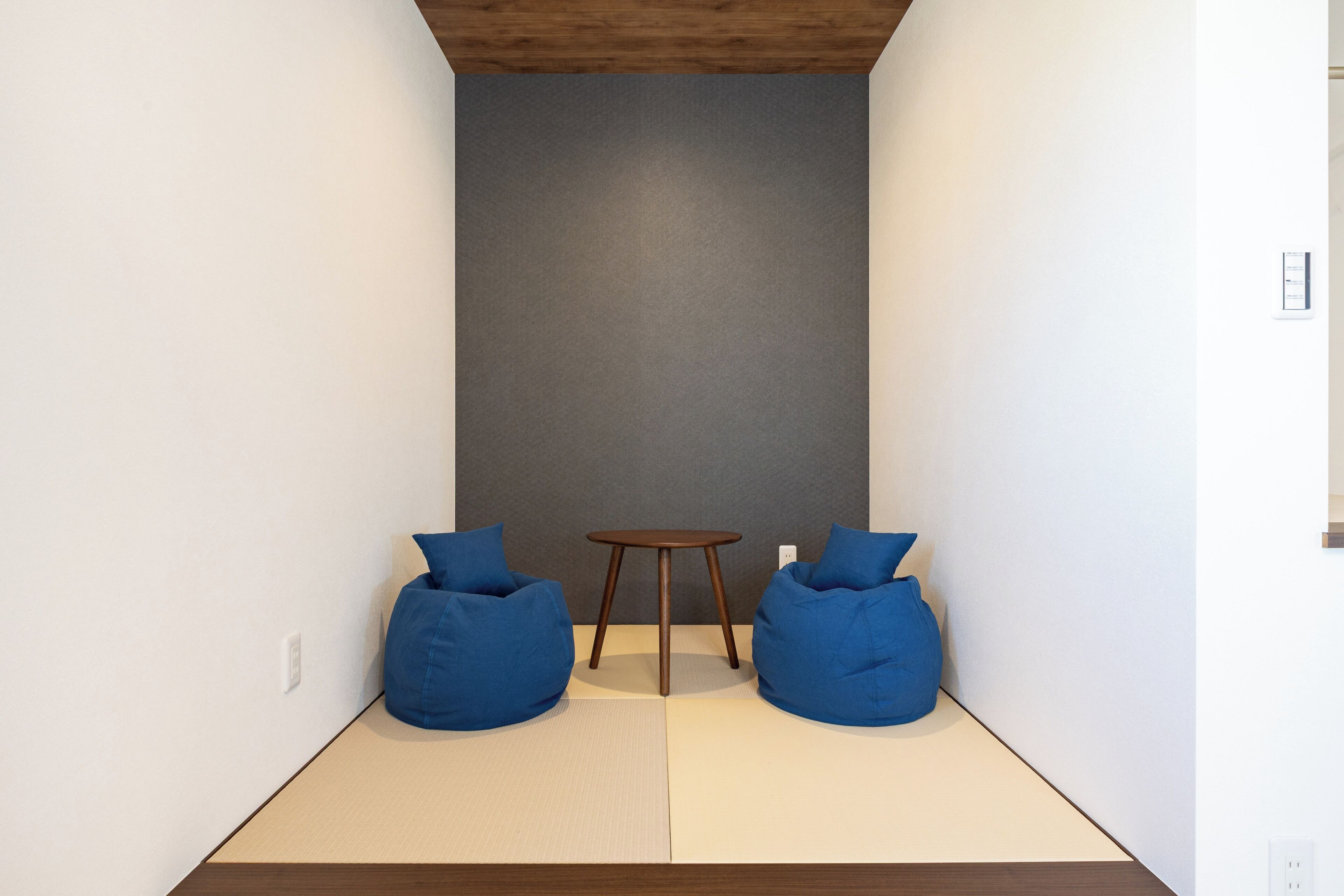 A minimalist room with two blue bean bags, a small round table, and a tatami mat floor.