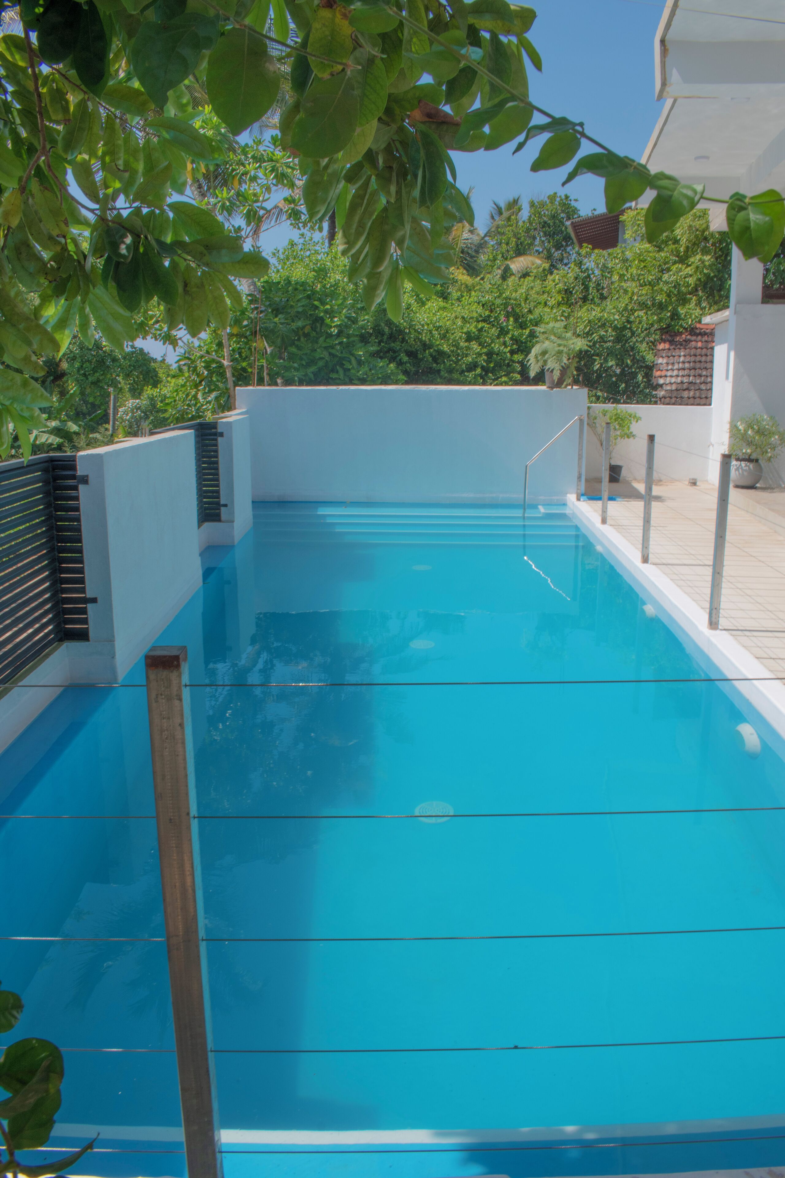 Une piscine rectangulaire à l’eau d’un bleu cristallin, entourée d’un mur blanc et de rampes en métal.
