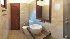 A bathroom with a wooden door, a toilet, a sink with a mirror, and a towel rack. - Caliza Unawatuna by Sea Cloud (Galle)
