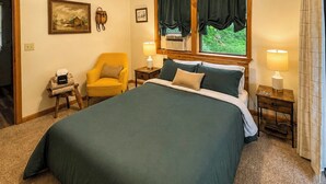 Quarto com uma cama grande, uma cadeira, duas mesas de cabeceira e uma janela com cortinas.