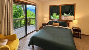 Quarto com cama grande, uma cadeira, janela com cortinas e ar condicionado.