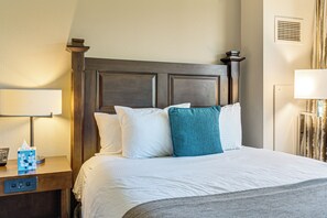 Una habitación de hotel con una cama grande, una mesita de noche con lámpara y un respiradero en la pared.