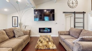 Una sala de estar con dos sofás, una mesa de centro, un televisor de pantalla plana montado en la pared, un reloj y una puerta corredera.